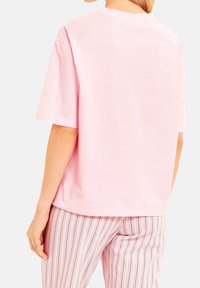 Kort rosa bomullströja med korta ärmar, rund halsringning och avslappnad passform, ihop med rosa och vita randiga byxor.