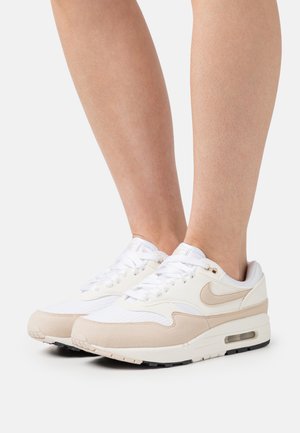 Ženske Nike Air Max 1 tenisice imaju gornji dio od bijelog tekstila s bež suženim detaljima. Imaju okrugli vrh, vezanje sprijeda i vidljivu zračnu jedinicu u potplatu.
