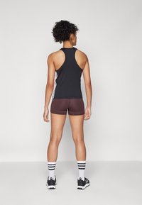 Svart idrottströja med racerback-design, kombinerad med bruna shorts. Modellen bär svarta skor och strumpor med svart/vit rand.