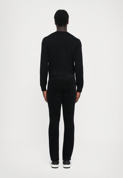 Sort langærmet skjorte og mørke kordfløjl bukser. Stoffet er glat; skjorten har en rund halsudskæring, og bukserne har baglommer og lige snit.