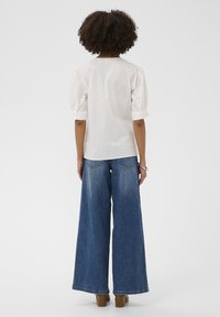 Bluză albă cu mâneci bufante, croială dreaptă, asortată cu blugi evazați din denim, cu spălare deschisă și buzunare la spate. Pantofi cu toc pătrat maro.