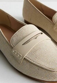 Mocasines beige con un upper de tela texturizada y una banda de cuero suave con acentos recortados. Diseño de bajo perfil con una puntera redondeada.