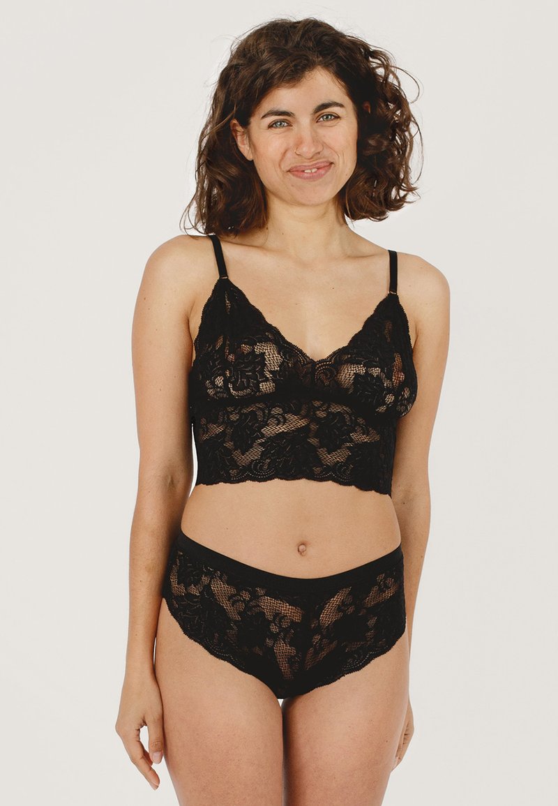 Zwarte kant bralette met bloemmotieven, verstelbare bandjes en bijpassende kanten string met een golvende rand. Zachte, doorschijnende textuur.
