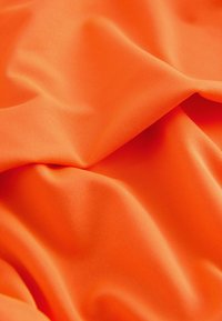 Heldere oranje stof met een gladde textuur, voorzien van zachte plooien en een licht geribbelde oppervlakte voor extra dimensie.