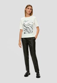 T-shirt blanche à manches courtes avec un motif de vagues argentées sur le devant, associé à un pantalon en cuir noir et des chaussures noires.