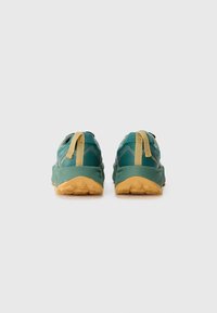 Green trail running shoes with textured fabric, rounded shape, yellow rubber sole, contrasting stitching, and pull tabs at the heel.