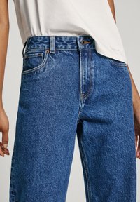 Blå denimjeans med avslappnad passform, hög midja, klassisk femficksdesign och kontrastsömmar. Matchas med en avslappnad vit t-shirt.