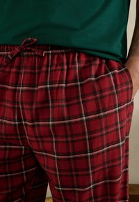 Pantaloni del pigiama in tessuto morbido con motivo a quadri rossi, linee bianche e verdi. Vita elastica con coulisse per una vestibilità regolabile.