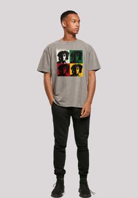 Graues T-Shirt mit grafischem Druck und lässigem Schnitt, das einen bunten, im Pop-Art-Stil gestalteten Druck eines Gesichts in Rot, Grün, Gelb und Schwarz zeigt. Schwarze Jogginghosen.