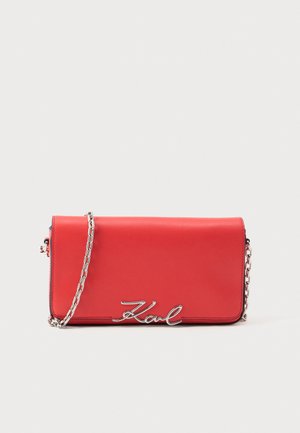 Red leather clutch purse with silver chain strap and silver "Karl" signature detail on front flap against white background.