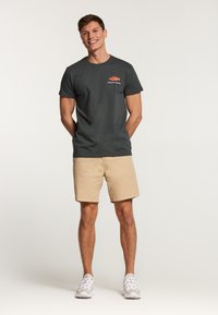 Camiseta de algodón gris oscuro con un gráfico de un pez y el texto "CATCH OF THE DAY", combinada con pantalones cortos caqui y zapatillas blancas.
