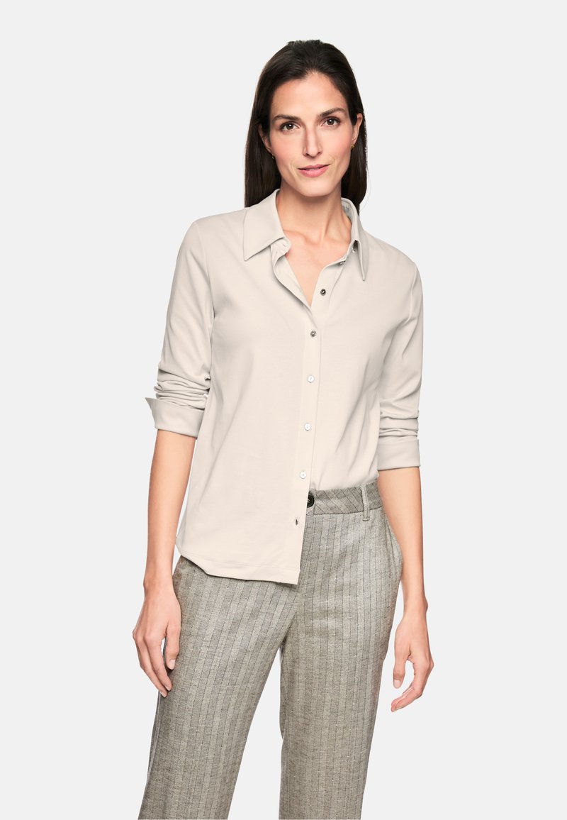 Light grey button-up shirt with a classic collar, long sleeves, and a soft texture, paired with patterned grey trousers.