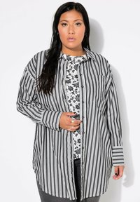 Camicia a righe bianca e nera, realizzata in un tessuto leggero, con maniche lunghe e una vestibilità rilassata. Lo strato interno presenta un motivo floreale.