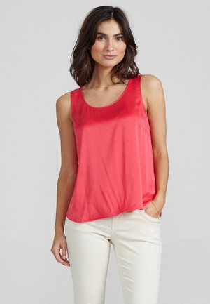 Top sin mangas de color coral, confeccionado en una tela suave, con un escote redondo y un corte relajado, combinado con pantalones de color claro.