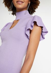 Fioletowa sukienka w prążki z wysokim kołnierzem i falbaniastymi krótkimi rękawami, podkreślająca dopasowaną sylwetkę i subtelną teksturę.