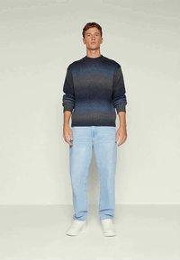 Camisola de malha com gradiente do azul escuro ao cinza, com punhos e bainha canelados, usada com jeans azul claro e ténis brancos. Design simples e casual.