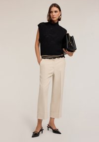 Top senza maniche in maglia nera con orlo scallop, abbinato a pantaloni a gamba larga beige. Gli accessori includono una borsa nera e tacchi a punta.