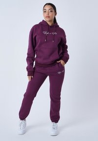 Conjunto de sudadera con capucha y pantalones de chándal en color púrpura, fabricado en una mezcla de algodón, que cuenta con puños elásticos, un bolsillo frontal y gráficos en la sudadera y los pantalones.