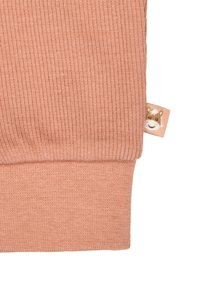 Ribbeliger, weicher pinker Stoff mit umgeschlagenem Saum. Enthält ein kleines Etikett mit einem lächelnden Cartoon-Tier. Glatte Textur, warme Ausstrahlung.