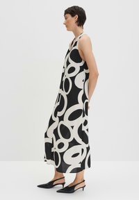 Schwarzes und weißes ärmelloses Kleid mit einem auffälligen kreisförmigen Muster, bestehend aus leichtem Stoff mit lockerer Passform, kombiniert mit schwarzen Slingback-Pumps.