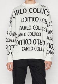 Suéter de punto blanco con texto negro repetido "CARLO COLUCCI" en varias orientaciones. Cuello redondo y puños acanalados.