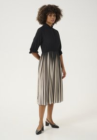 Čierny top s volánovým výstrihom a 3/4 rukávmi, skombinovaný s plynulou plisovanou sukňou s čierno-krémovými vertikálnymi pruhmi. Čierne podpätky.