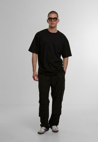Svart oversized T-skjorte med kortermet, sammen med svarte cargo-bukser med flere lommer. Fottøyet inkluderer hvite og svarte joggesko.