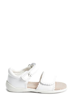 Sandale blanche pour enfants avec des brides Velcro, détail fleur sur la bride de cheville, et une semelle intérieure beige matelassée avec de petits points blancs.