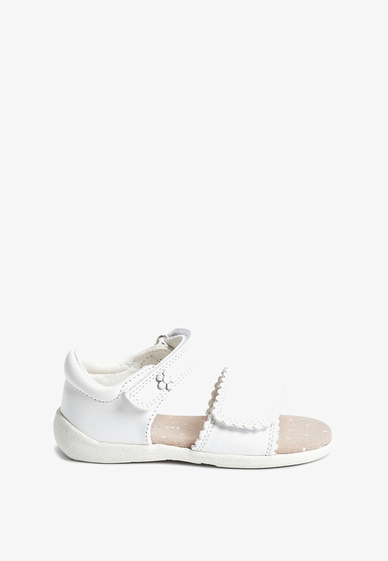 Sandale blanche pour enfants avec des brides Velcro, détail fleur sur la bride de cheville, et une semelle intérieure beige matelassée avec de petits points blancs.