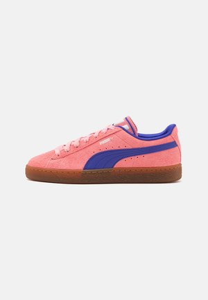 Lage sneaker met roze suède bovenwerk, blauwe Puma-streep, gumrubberen zool en roze veters op een witte achtergrond.