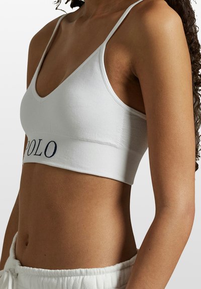 Bílá bavlněná braletka se střihem do V, úzkými ramínky a širokým pruhem s námořnicky modrým nápisem "POLO". Hladký povrch.