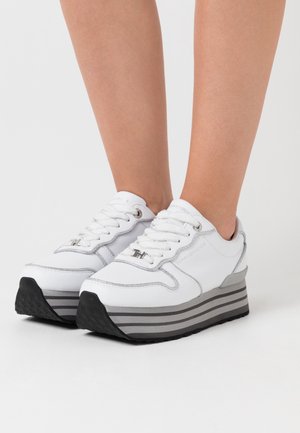 Bílé platformové tenisky se šedým pruhováním, koženým svrškem, šněrováním a stříbrnými akcenty na jazyku a po stranách. Černá gumová podešev.