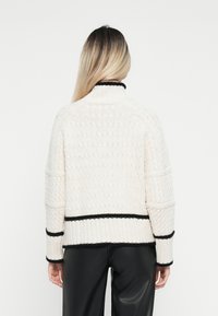 Chunky stickad tröja i off-white med ett texturerat mönster, med svarta accenter vid kragen och nederkanten, samt ribbade ärmslut.