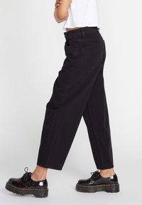 Zwarte high-waisted jeans met een relaxed fit, rechte pijpen en twee achterzakken. Gecombineerd met glanzende zwarte plateau schoenen.