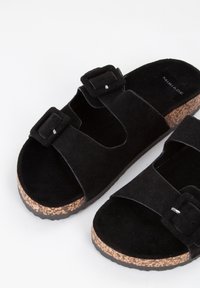 Sorte ruskindssandaler med to justerbare spænder, kork-vedge sål og tekstureret gummisål. Ingen fremtrædende mønstre eller accessories.