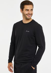 Sort langærmet T-shirt i blødt stof med rund halsudskæring, der har et lille hvidt logo på venstre bryst og tætsiddende ærmer.