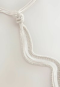 Silberfarbene Halskette mit mehreren Strängen, einem geknoteten Mittelpunkt, filigraner Perlenarbeit und einer glatten, strukturierten Oberfläche.