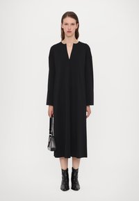 Black long-sleeve dress with a V-neck, flowing silhouette, and textured fabric; paired with black ankle boots featuring silver accents.