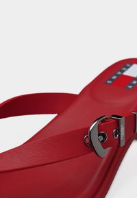 Κόκκινο σανδάλι με ρυθμιζόμενο μαύρο μεταλλικό πόρπη και λογότυπο Tommy Jeans, με υφασμένη εσωτερική σόλα και ριγέ έμβλημα του εμπορικού σήματος στη φτέρνα.