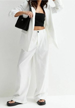 Bílý oversize blazer, černý cropped top a volné bílé kalhoty. Černá kabelka s hladkým povrchem. Silné černé platformové sandály.