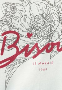 Biała bawełniana tkanina z szarym wzorem kwiatowym, na którym nałożone jest czerwone efektywne napisy "Bison" i akcent w kształcie serca.