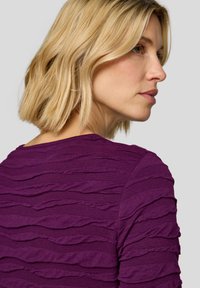 Lila Oberteil aus strukturiertem Stoff mit schichtigem, wellenförmigem Design. Verfügt über einen Rundhalsausschnitt und kurze Ärmel.