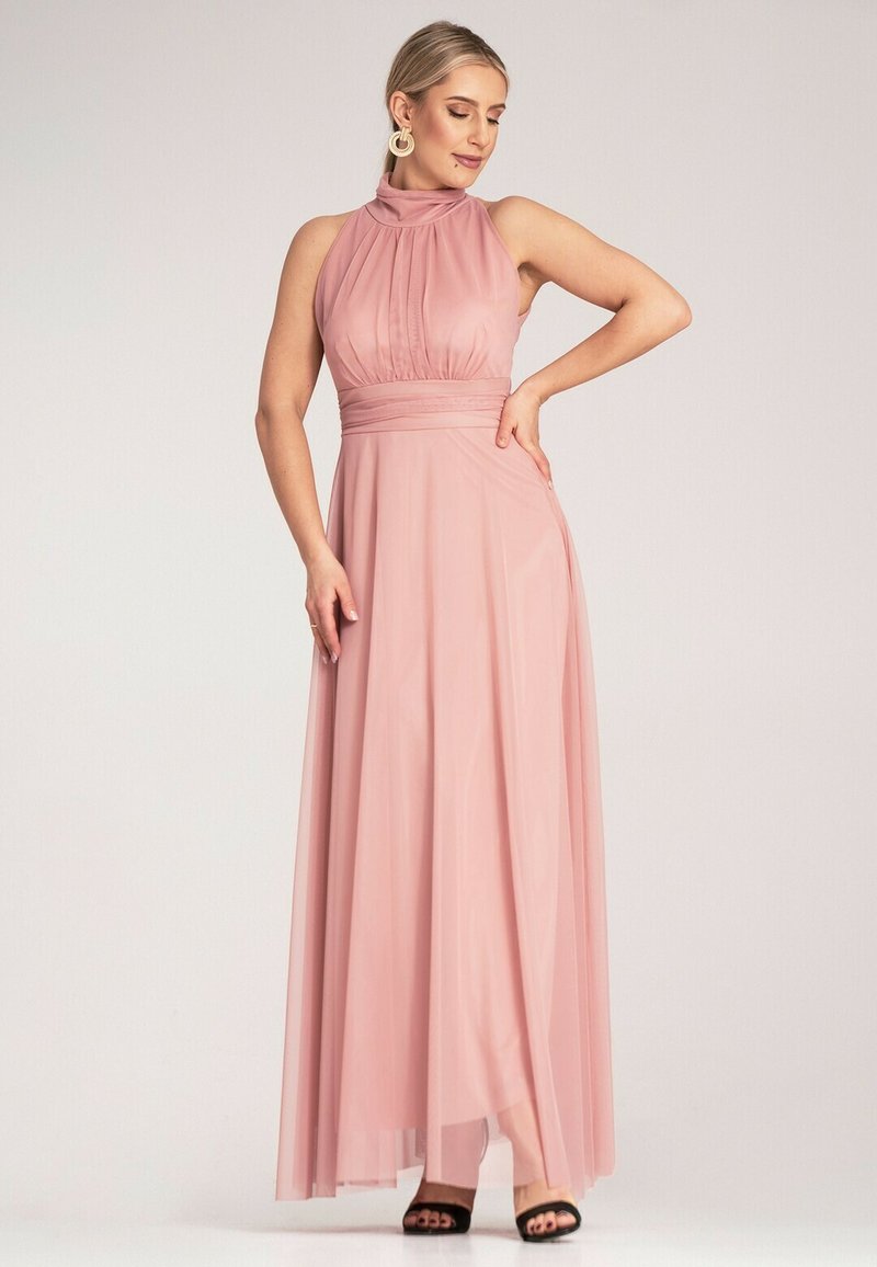Maxi sukienka z miękkiego różowego materiału z wysokim kołnierzem, plisowanym gorsetem i dopasowanym stanem, zwiewną spódnicą i subtelnym rozporkiem po bokach. Czarne obcasy.