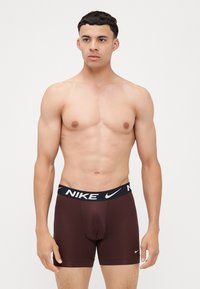 Hnedé boxerky Nike s čiernym elastickým pásom s logom Nike. Vyrobené z hladkej, elastickej látky pre pohodlie.