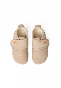 Beige stoffen kinderschoenen met een gestructureerde ondergrond, ronde neus, klittenbandsluiting en een klein merklabel aan de zijkant.