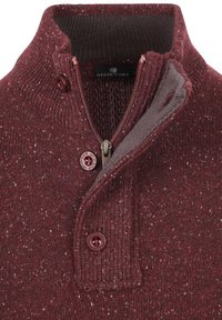 Bordeauxkleurige gebreide trui met een hoge kraag, ritssluiting aan de voorkant en een gestructureerd, gespikkeld patroon. Heeft een knoopsluiting en een merkembleem.