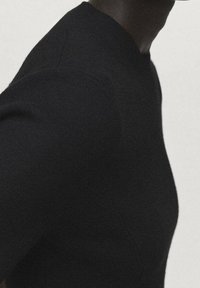 Haut en maille noire avec un col rond, une coupe ajustée et une texture côtelée subtile ; doté d'une finition lisse et de détails sans coutures.