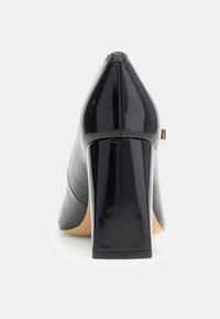 Scarpa col tacco alto in pelle verniciata nera con punta affusolata e tacco spesso. Texture liscia con dettagli di cuciture sottili lungo il lato.