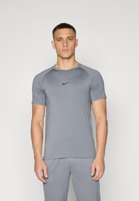 Camiseta deportiva gris de manga corta, con cuello redondo y logo negro de Nike en el pecho; diseño ajustado hecho de material ligero y transpirable.