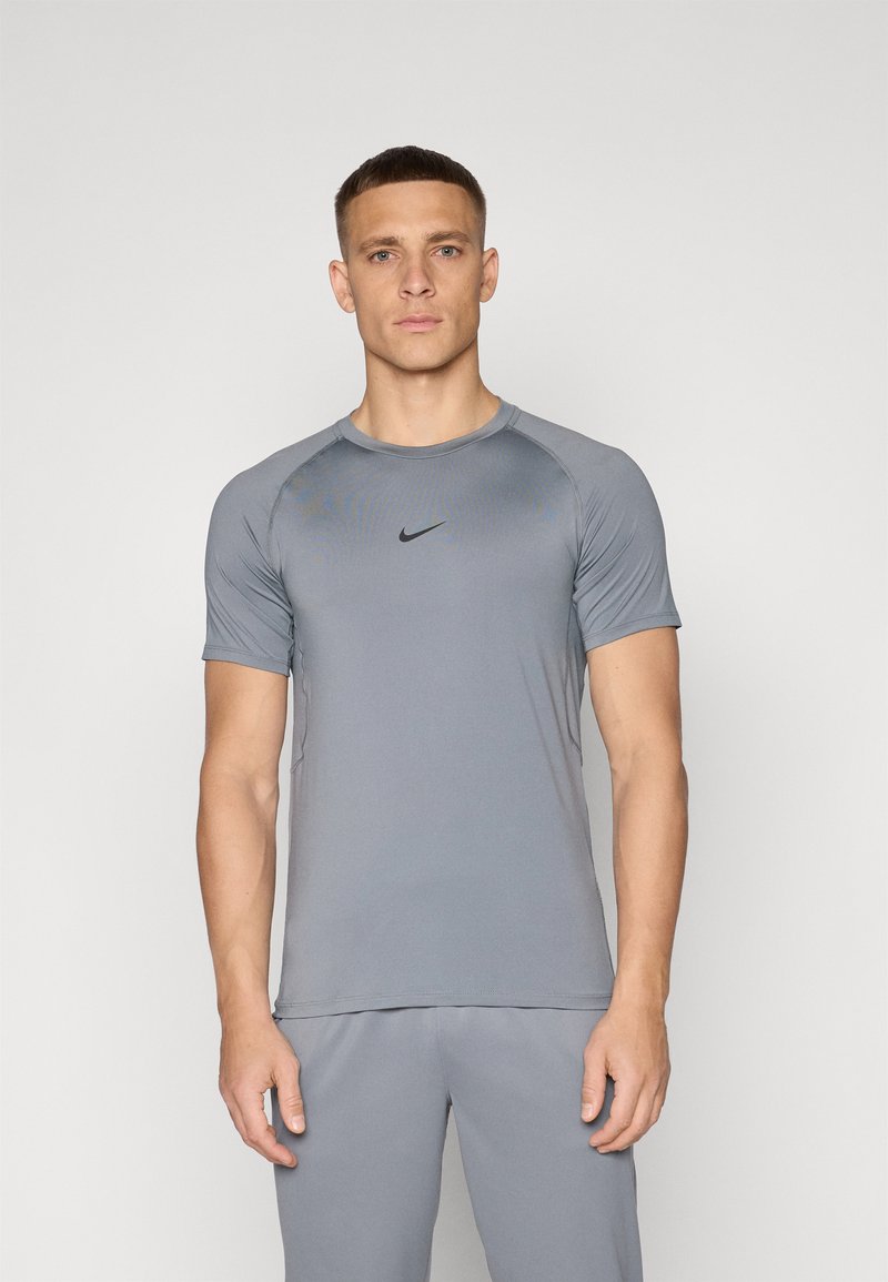 Camiseta deportiva gris de manga corta, con cuello redondo y logo negro de Nike en el pecho; diseño ajustado hecho de material ligero y transpirable.